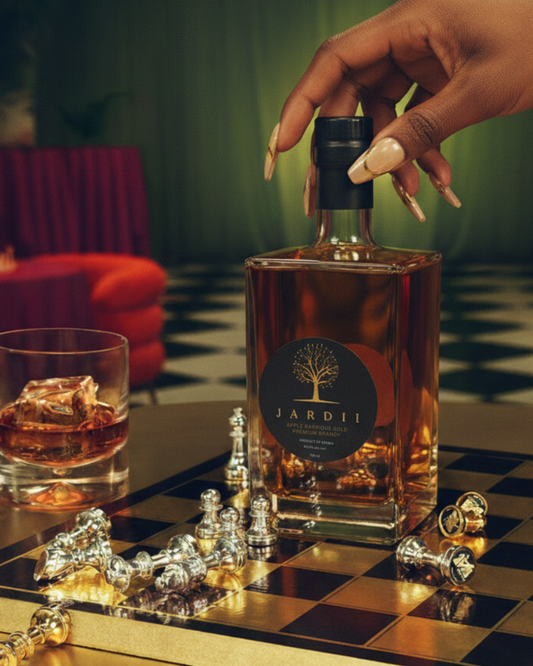 Hand reaching for JARDII premium brandy bottle on chess board with whiskey glass and chess pieces